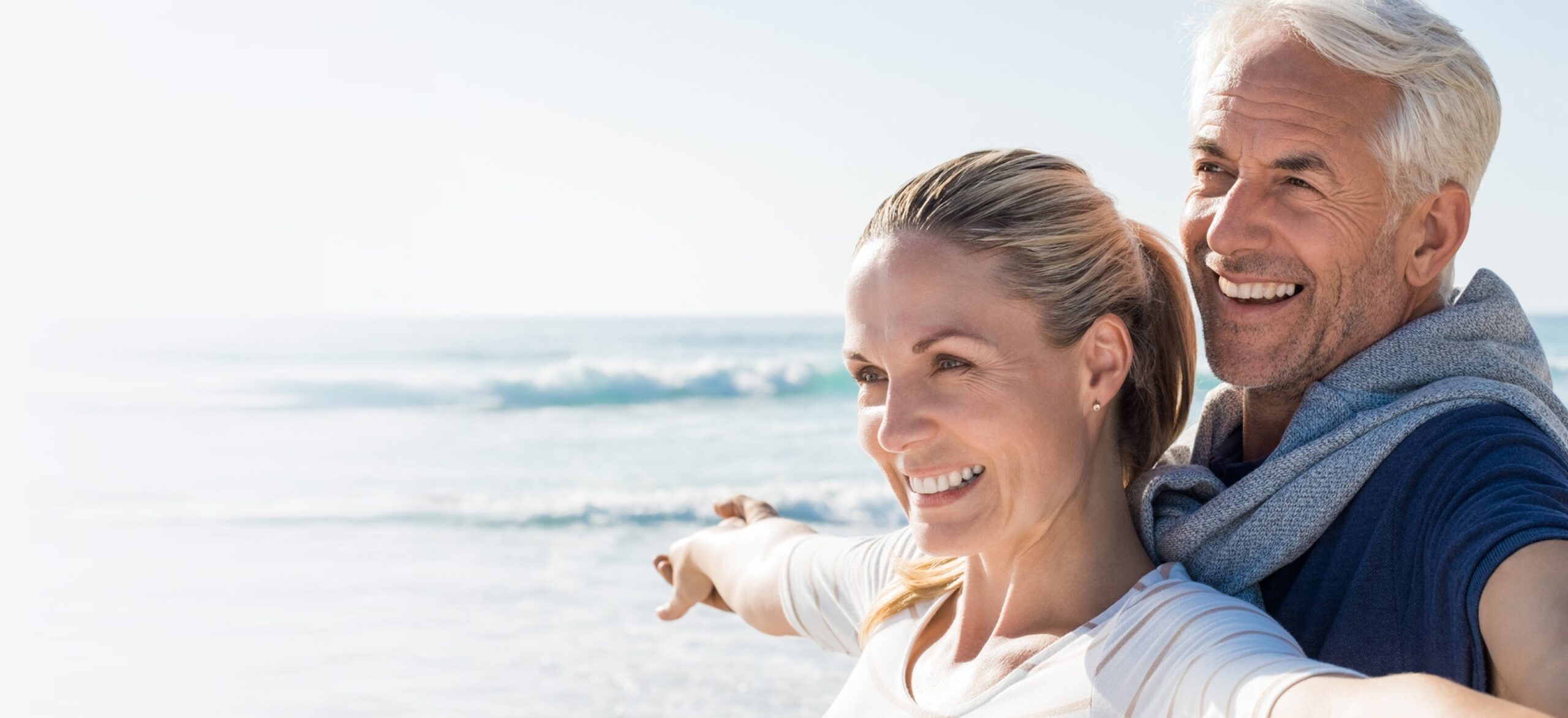 Happy Senior Couple Standing On Beach With Arms Outstretched And Looking Away